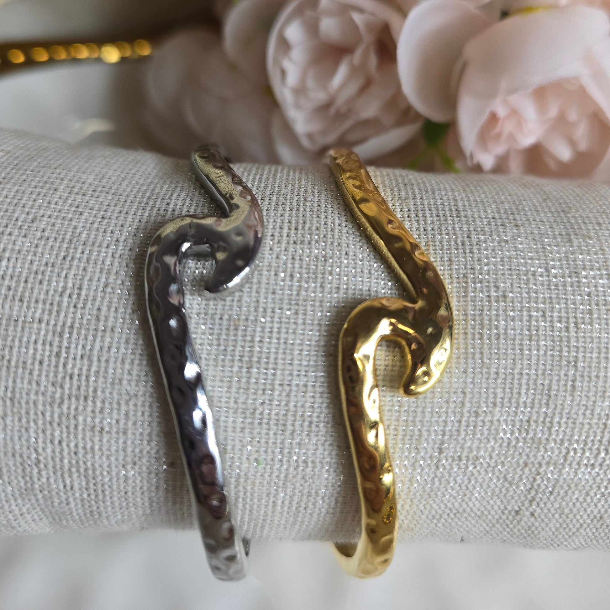Gold and silver snake-shaped rings on a textured surface with flowers in the background