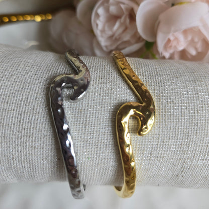 Gold and silver snake-shaped rings on a textured surface with flowers in the background