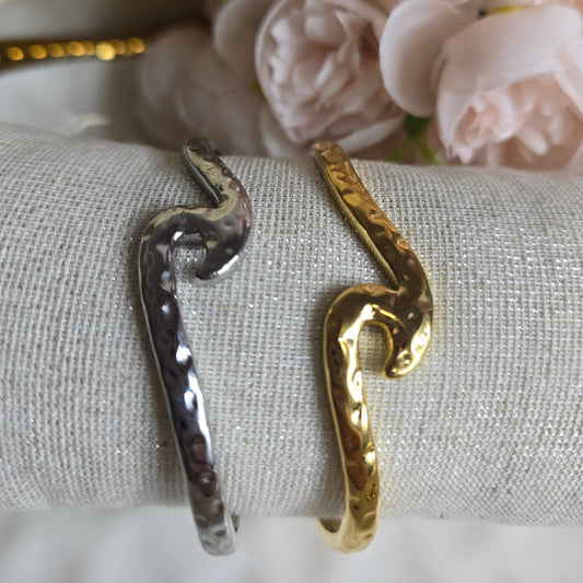 Gold and silver snake-shaped rings on a textured surface with flowers in the background