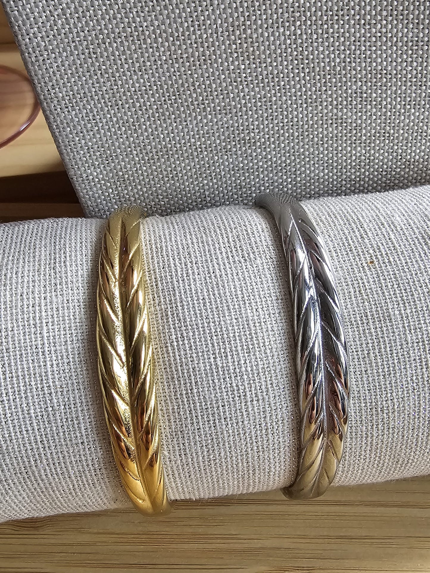 The Leaf Bangle from Art of Shine, shown in both gold and silver tone finishes, displayed on a linen cushion.